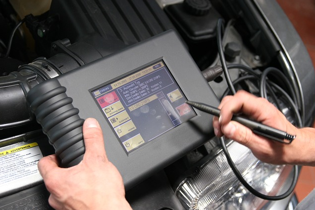 A person inspecting a digital device while checking the engine, focused on diagnostics and vehicle performance.